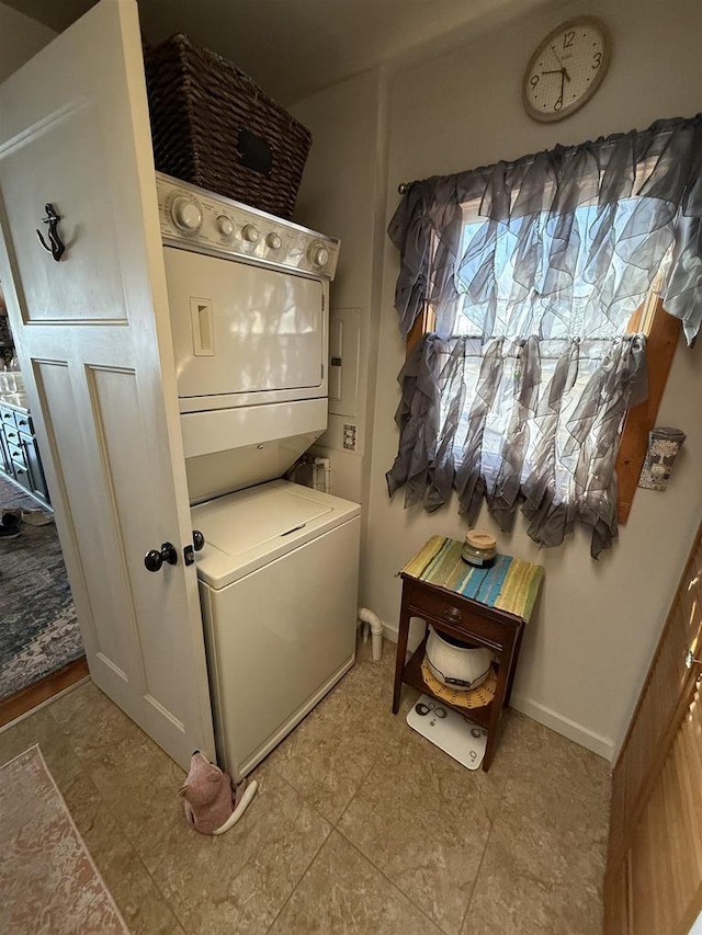 clothes washing area featuring baseboards, stacked washer and clothes dryer, and laundry area