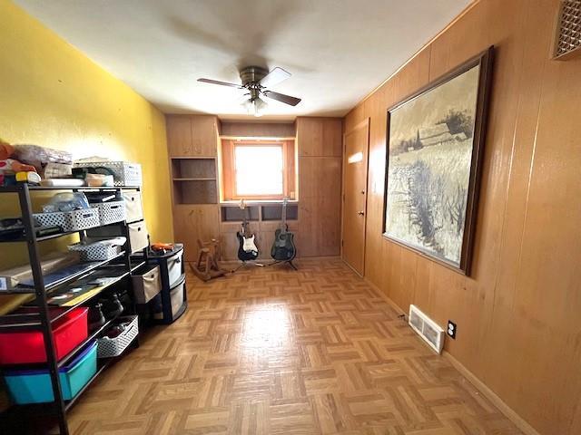 interior space featuring visible vents, baseboards, wooden walls, and a ceiling fan