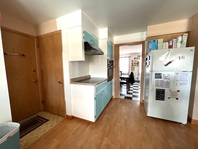 kitchen featuring black appliances, blue cabinetry, wood finished floors, and under cabinet range hood