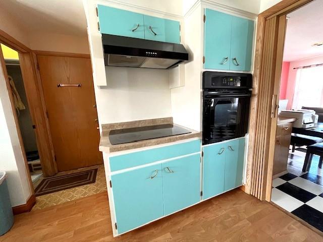 kitchen featuring black appliances, blue cabinets, light floors, and under cabinet range hood