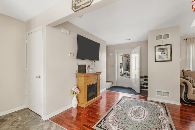 living area with visible vents, wood finished floors, baseboards, and a glass covered fireplace