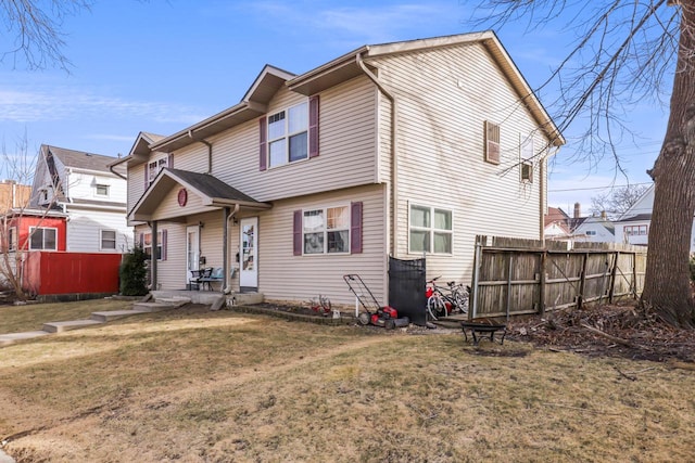 rear view of house with a lawn, an outdoor fire pit, and fence