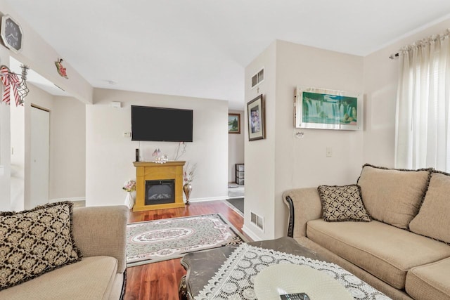 living area featuring visible vents, baseboards, a glass covered fireplace, and wood finished floors