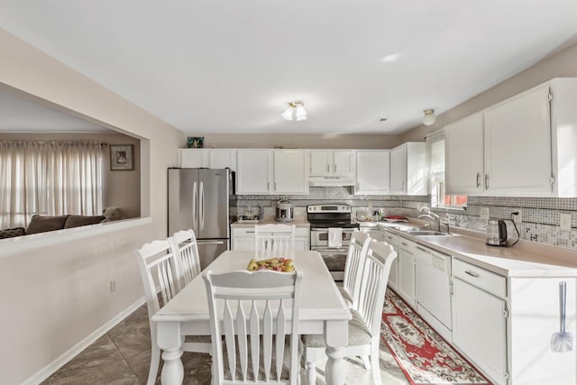 kitchen with light countertops, white cabinets, under cabinet range hood, appliances with stainless steel finishes, and tasteful backsplash