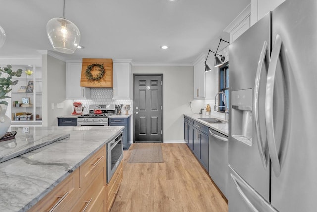 kitchen with light wood-style flooring, ornamental molding, a sink, appliances with stainless steel finishes, and tasteful backsplash