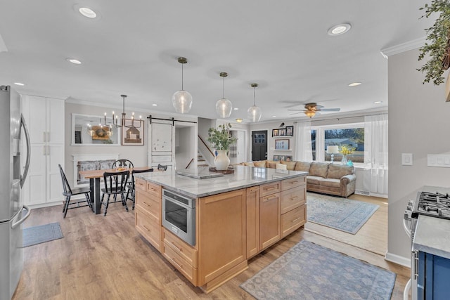 kitchen with light wood-type flooring, a barn door, stainless steel appliances, crown molding, and ceiling fan