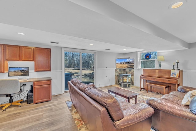 living room with light wood-style flooring, visible vents, a wood stove, and wainscoting