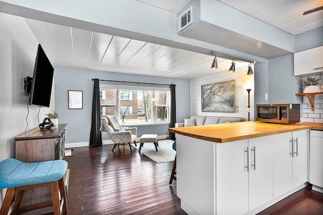 kitchen with stainless steel microwave, visible vents, white cabinetry, wood counters, and dark wood-style flooring