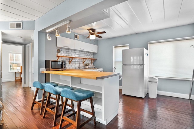 kitchen featuring stainless steel microwave, backsplash, visible vents, butcher block countertops, and freestanding refrigerator