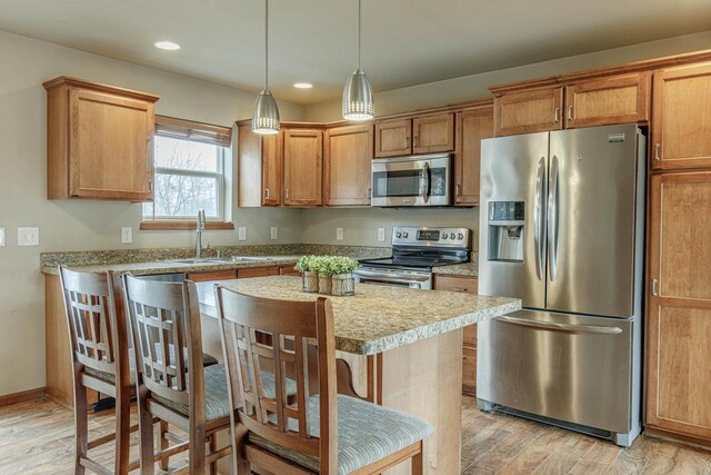 kitchen featuring light wood finished floors, appliances with stainless steel finishes, a kitchen island, and a sink