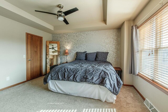 carpeted bedroom featuring a tray ceiling, baseboards, visible vents, and wallpapered walls