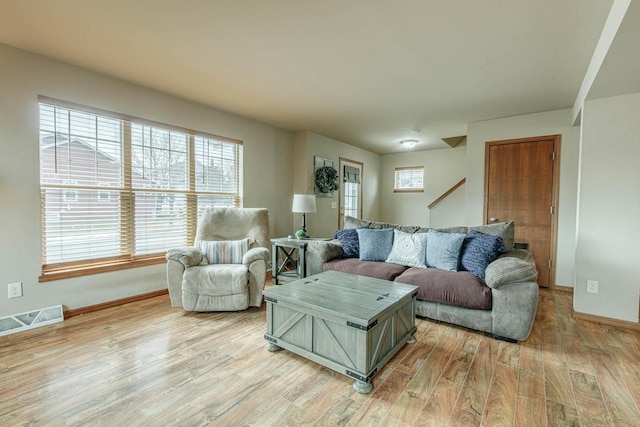 living area with stairs, baseboards, visible vents, and light wood-type flooring