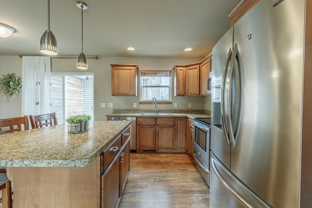 kitchen featuring a kitchen island, pendant lighting, light wood-style floors, stainless steel appliances, and a sink