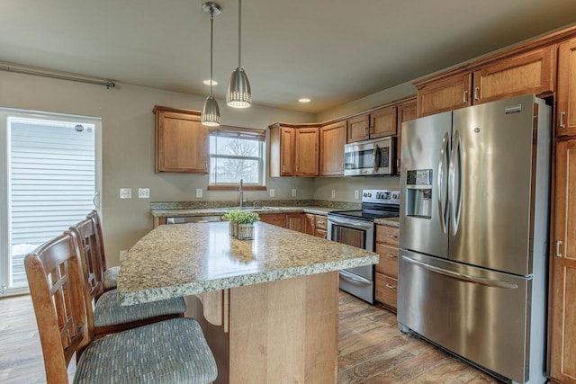 kitchen with a kitchen island, light countertops, light wood-style flooring, appliances with stainless steel finishes, and a sink