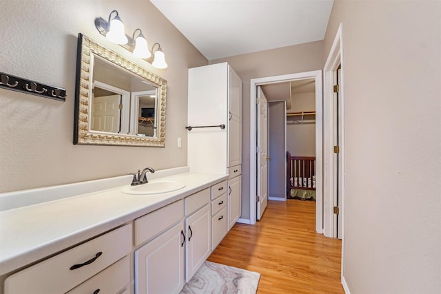 bathroom with a walk in closet, wood finished floors, and vanity