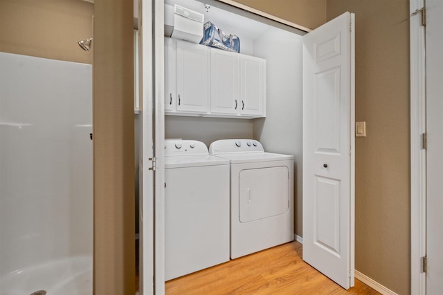 laundry room featuring baseboards, cabinet space, light wood-style floors, and washer and clothes dryer