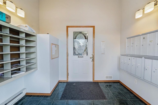 foyer with mail area, dark tile patterned flooring, baseboards, and a baseboard radiator