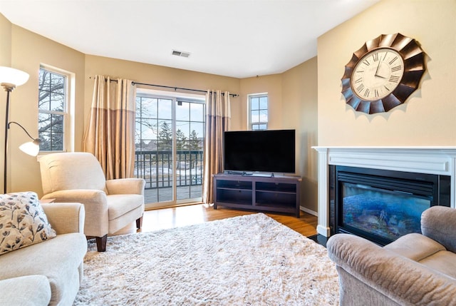 living area featuring visible vents, a fireplace with flush hearth, and wood finished floors