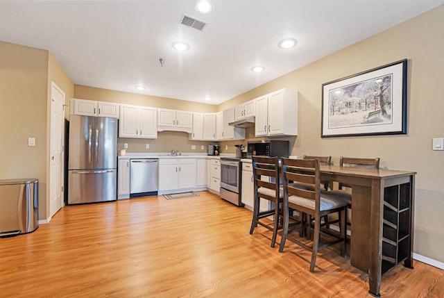 kitchen with visible vents, light wood-style floors, under cabinet range hood, appliances with stainless steel finishes, and white cabinetry