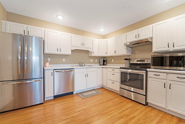 kitchen with light wood finished floors, under cabinet range hood, stainless steel appliances, white cabinetry, and a sink