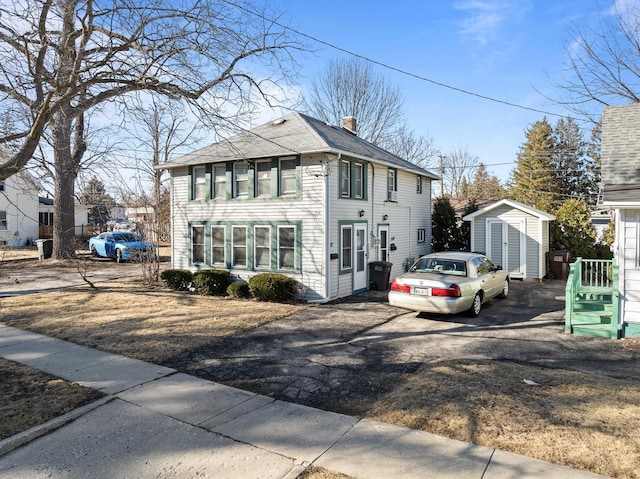 view of front facade featuring an outbuilding, a storage shed, a chimney, and a shingled roof