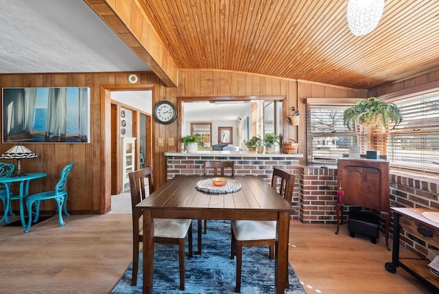 dining space featuring vaulted ceiling, wooden walls, and wood finished floors