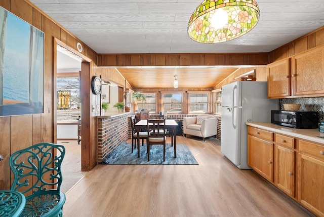 kitchen featuring freestanding refrigerator, wooden walls, light wood-style floors, and black microwave