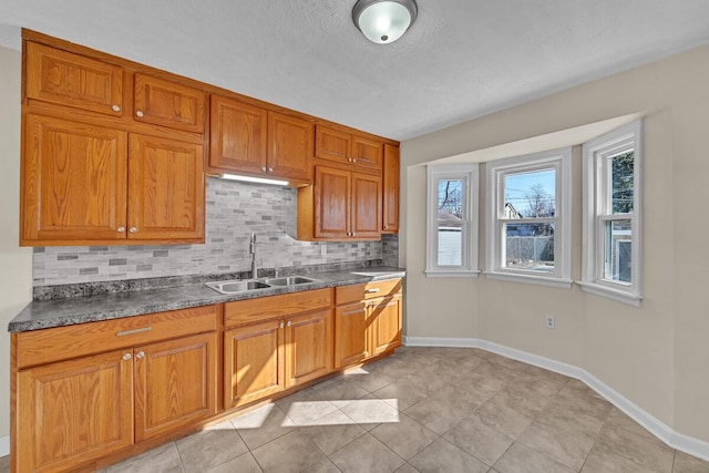 kitchen with dark countertops, brown cabinets, backsplash, and a sink