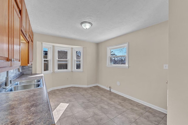 unfurnished dining area featuring light tile patterned floors, a textured ceiling, baseboards, and a sink