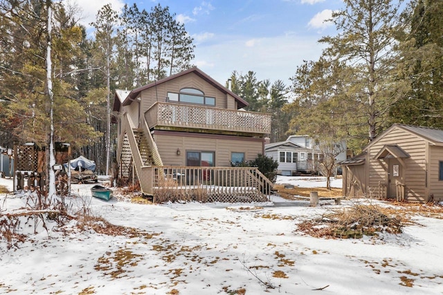 snow covered house with a wooden deck, an outbuilding, and stairway