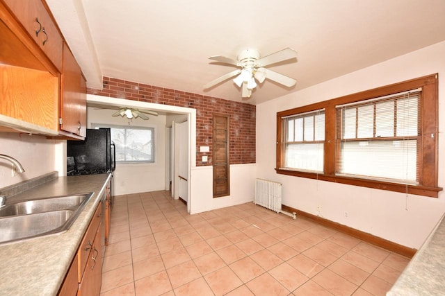 kitchen featuring radiator, a ceiling fan, brick wall, light tile patterned flooring, and a sink