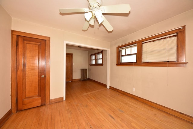 empty room with ceiling fan, radiator, light wood-type flooring, and baseboards