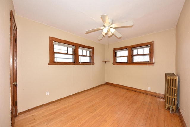 unfurnished room featuring a ceiling fan, radiator heating unit, baseboards, and light wood-type flooring