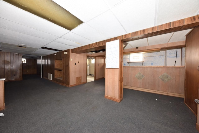 below grade area featuring carpet flooring, visible vents, a paneled ceiling, and wooden walls