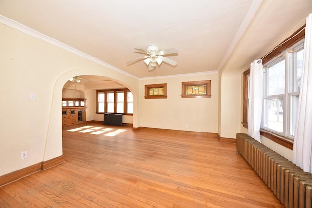 unfurnished living room featuring radiator heating unit, arched walkways, ceiling fan, ornamental molding, and light wood-type flooring