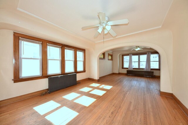 unfurnished room with hardwood / wood-style flooring, radiator heating unit, baseboards, and arched walkways