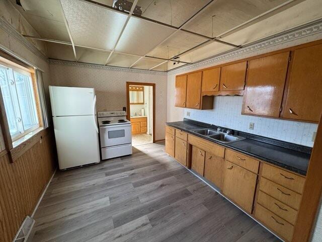 kitchen with a sink, white appliances, dark countertops, and wood finished floors