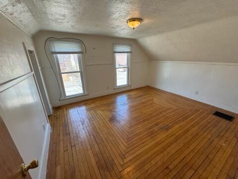 bonus room with visible vents, a textured ceiling, wood-type flooring, and vaulted ceiling