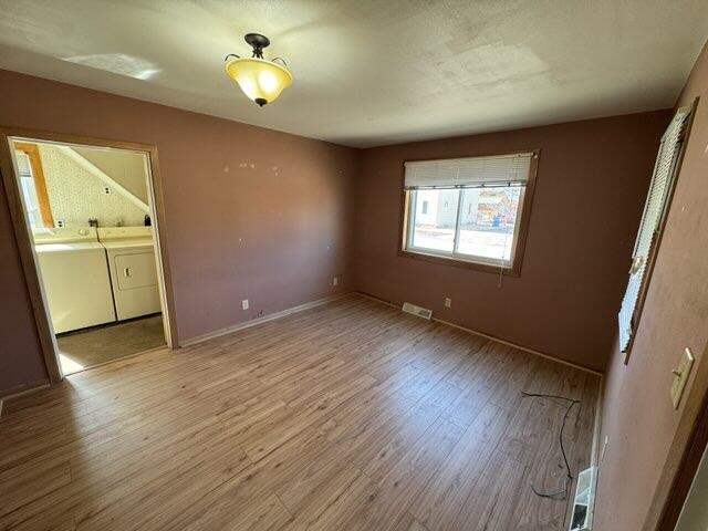 unfurnished bedroom with light wood-type flooring, visible vents, independent washer and dryer, connected bathroom, and baseboards