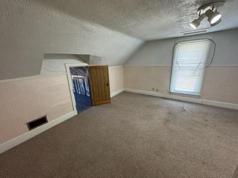 bonus room with vaulted ceiling, carpet flooring, baseboards, and a textured ceiling