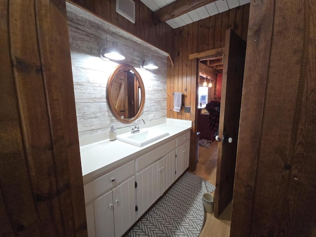 bathroom featuring wooden walls, beamed ceiling, vanity, and visible vents