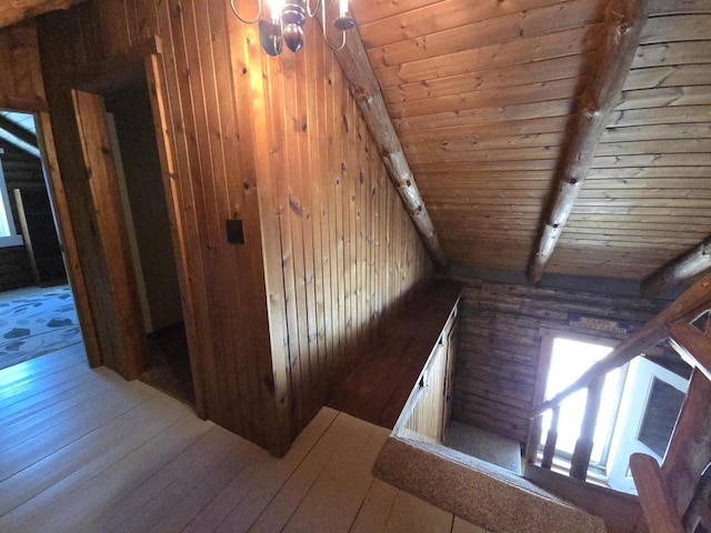 stairway with wooden walls, a chandelier, beamed ceiling, wooden ceiling, and hardwood / wood-style flooring