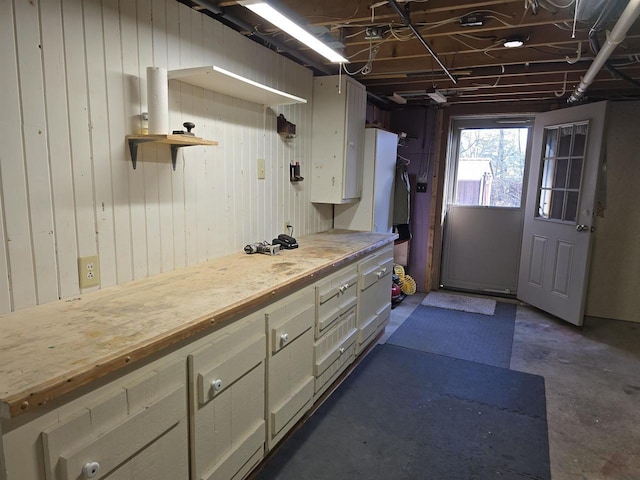 kitchen featuring open shelves, unfinished concrete flooring, butcher block countertops, and white cabinetry