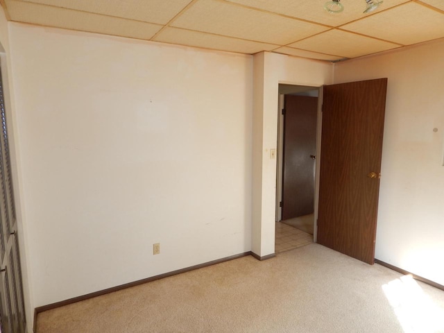 empty room featuring a paneled ceiling, light carpet, and baseboards