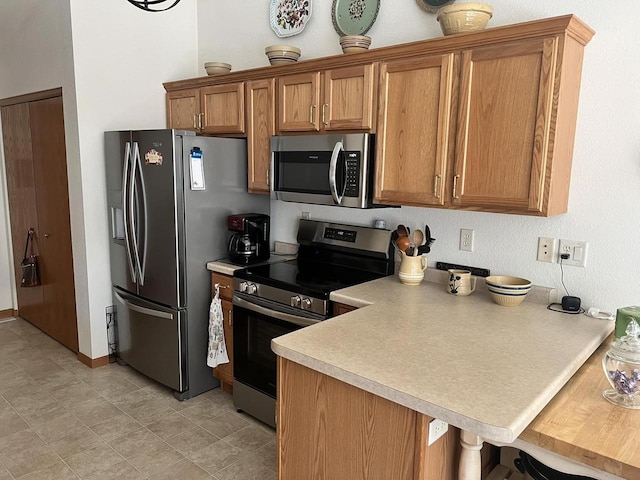 kitchen featuring a breakfast bar, a peninsula, stainless steel appliances, light countertops, and brown cabinets