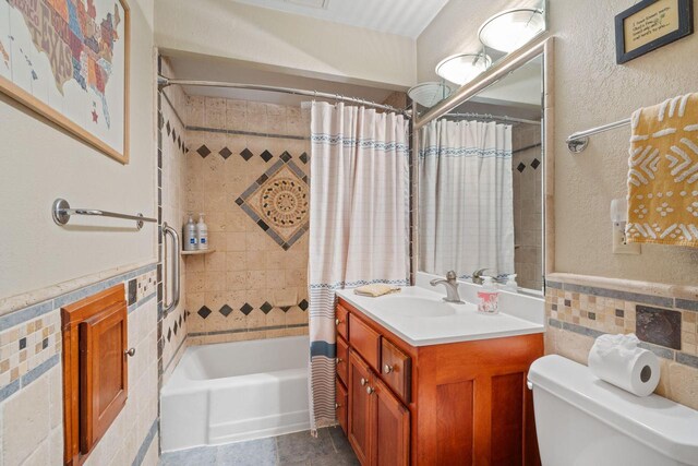 bathroom featuring a wainscoted wall, shower / bath combo with shower curtain, toilet, and tile walls