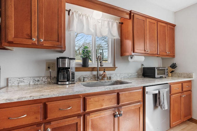 kitchen with light stone counters, brown cabinetry, a toaster, a sink, and dishwasher