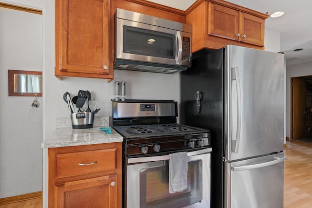 kitchen with light stone counters, brown cabinets, stainless steel appliances, and light wood-style flooring