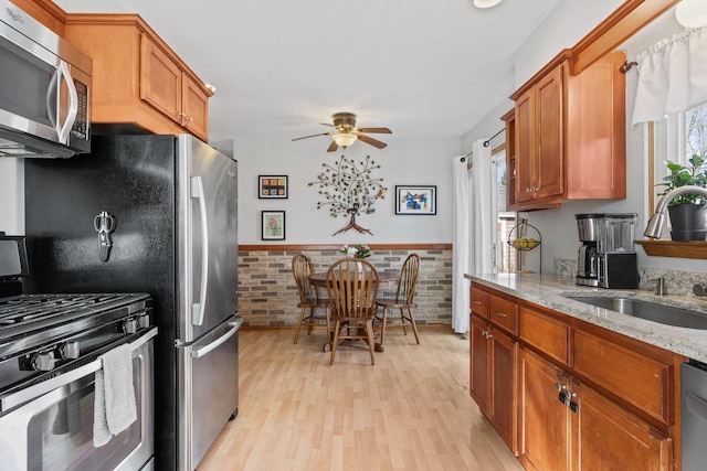 kitchen with a sink, light wood-type flooring, appliances with stainless steel finishes, and brown cabinetry