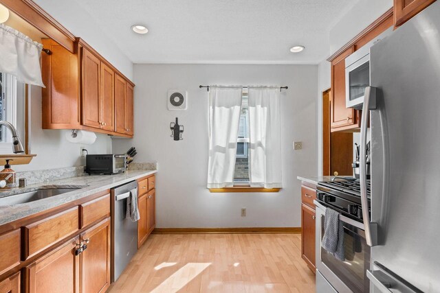 kitchen featuring light stone countertops, brown cabinets, light wood-style flooring, stainless steel appliances, and a sink